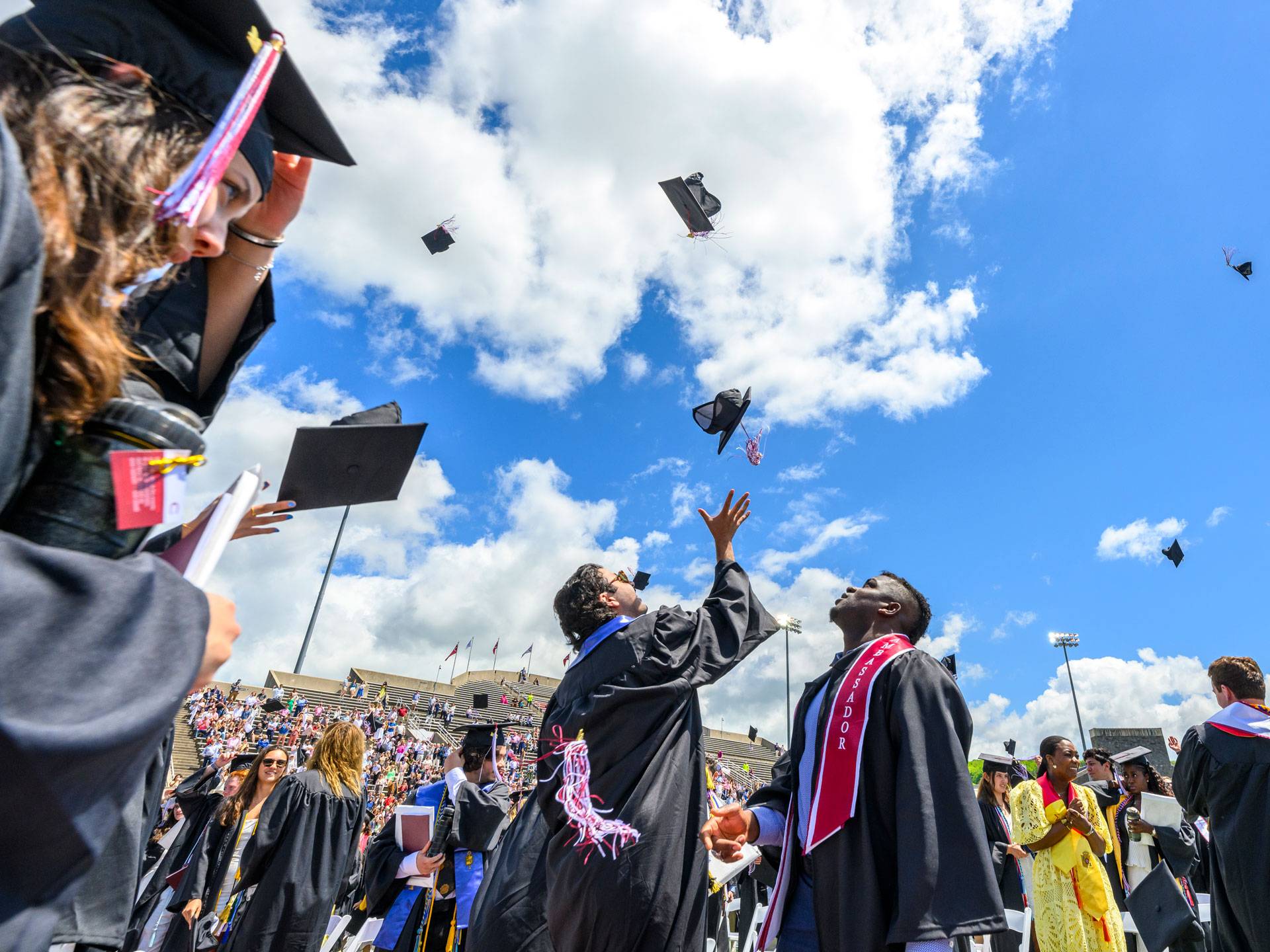 Two graduates in gowns throw their caps into the blue sky.