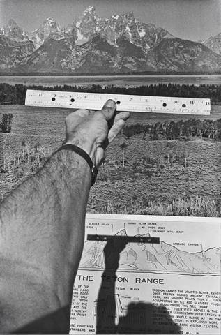 Arm holding ruler out to horizon with mountains