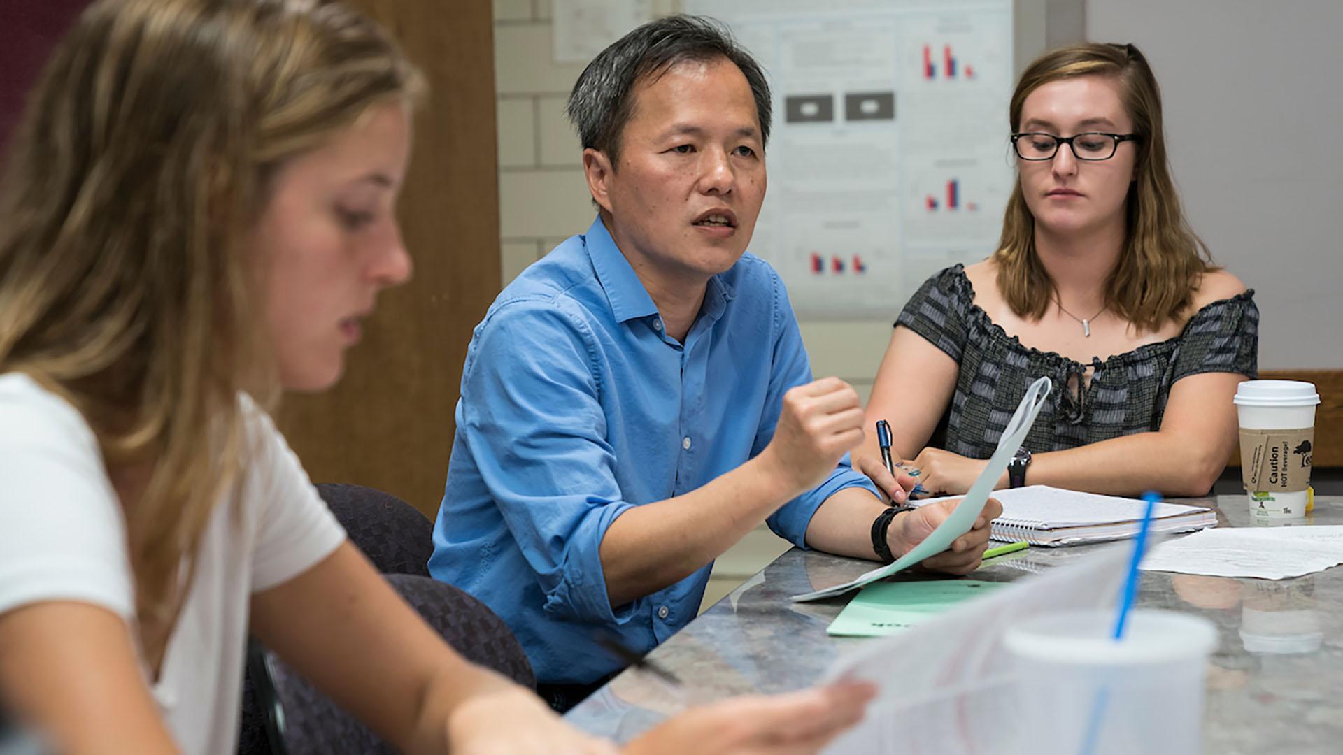Professor Wan-Chun Liu speaks with a small group of students at a table.