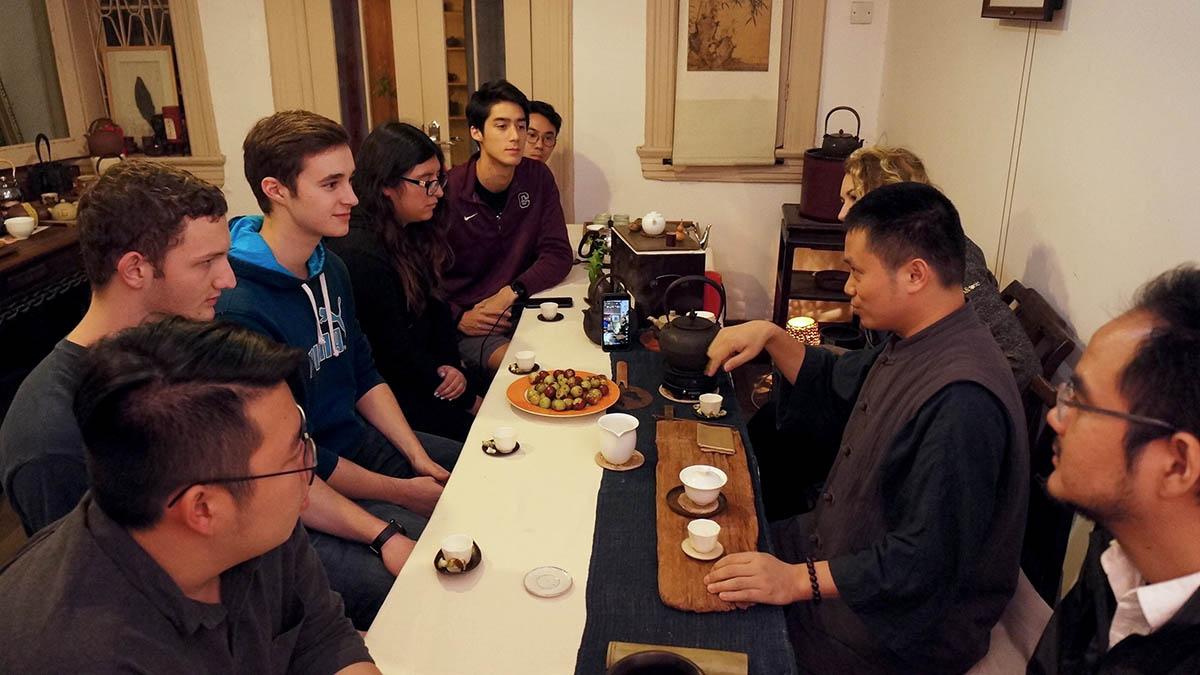 Students listen attentively to man with tea set.