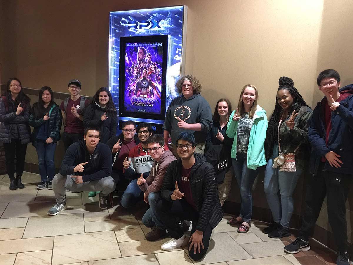AMS students pose with the Avengers: Endgame poster outside the theater
