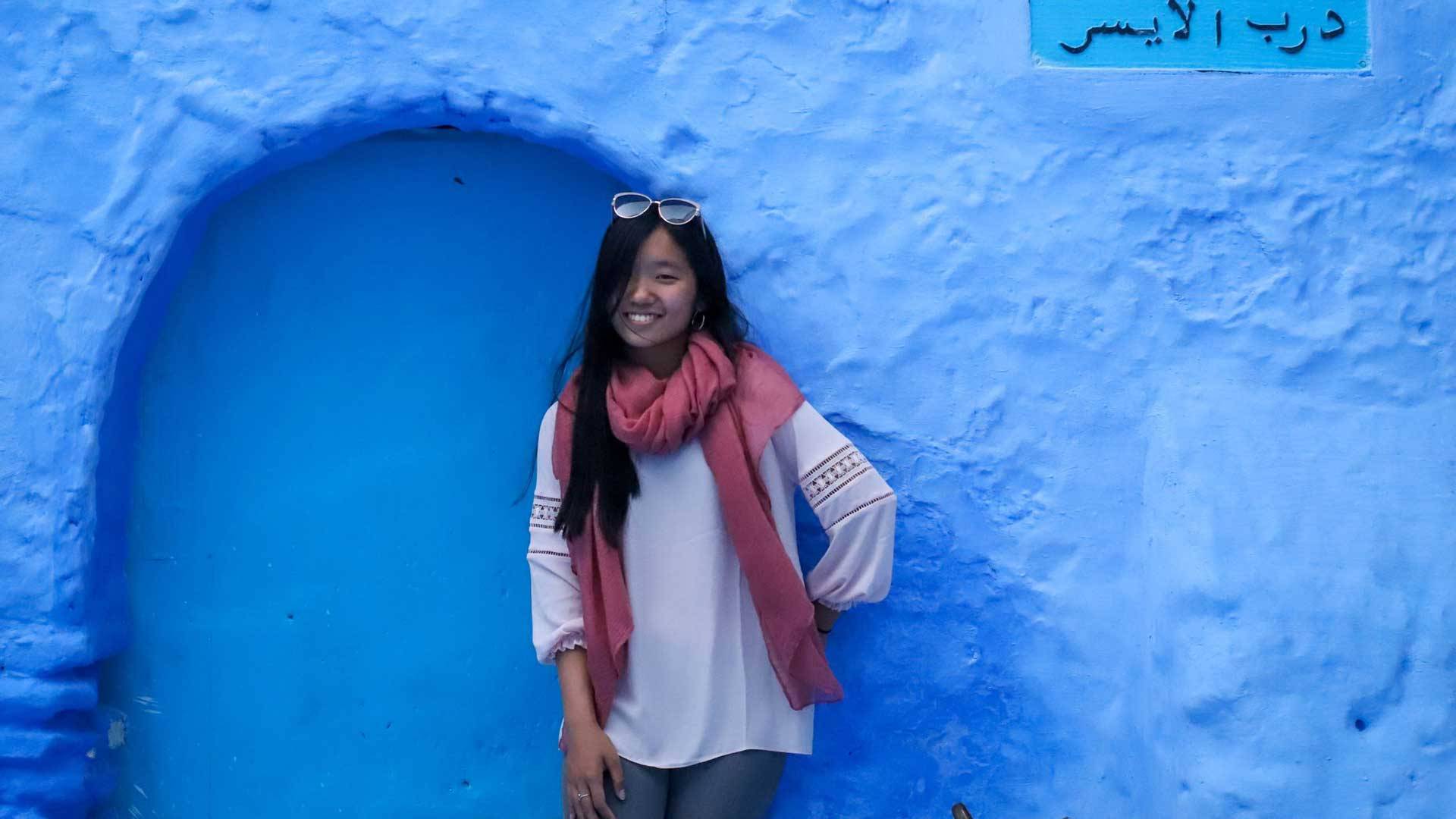 Justine Hu leans against a blue wall with a sign in Arabic on it