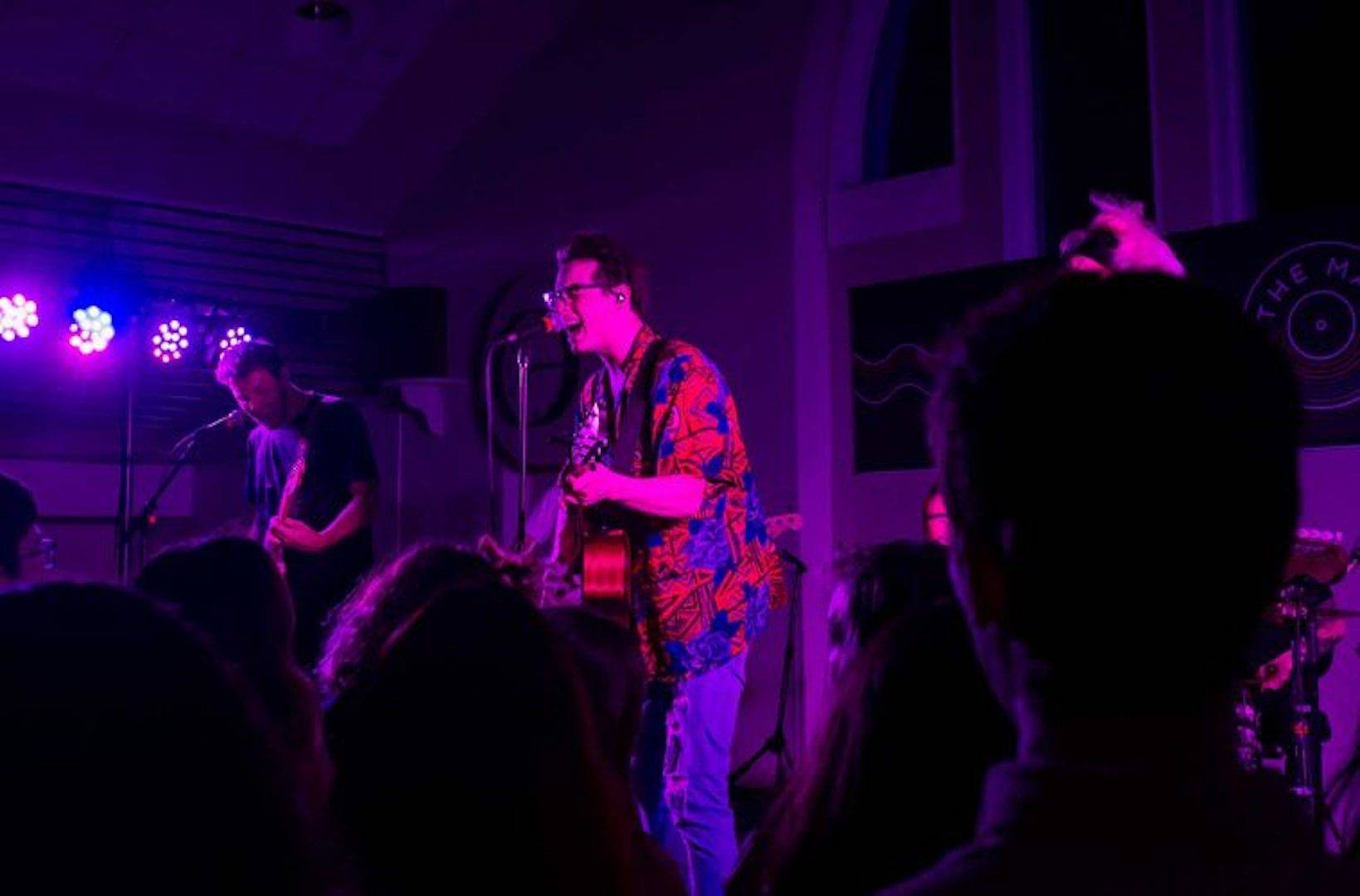 Male singer sings into mic during an intimate, darkly lit pop-rock performance