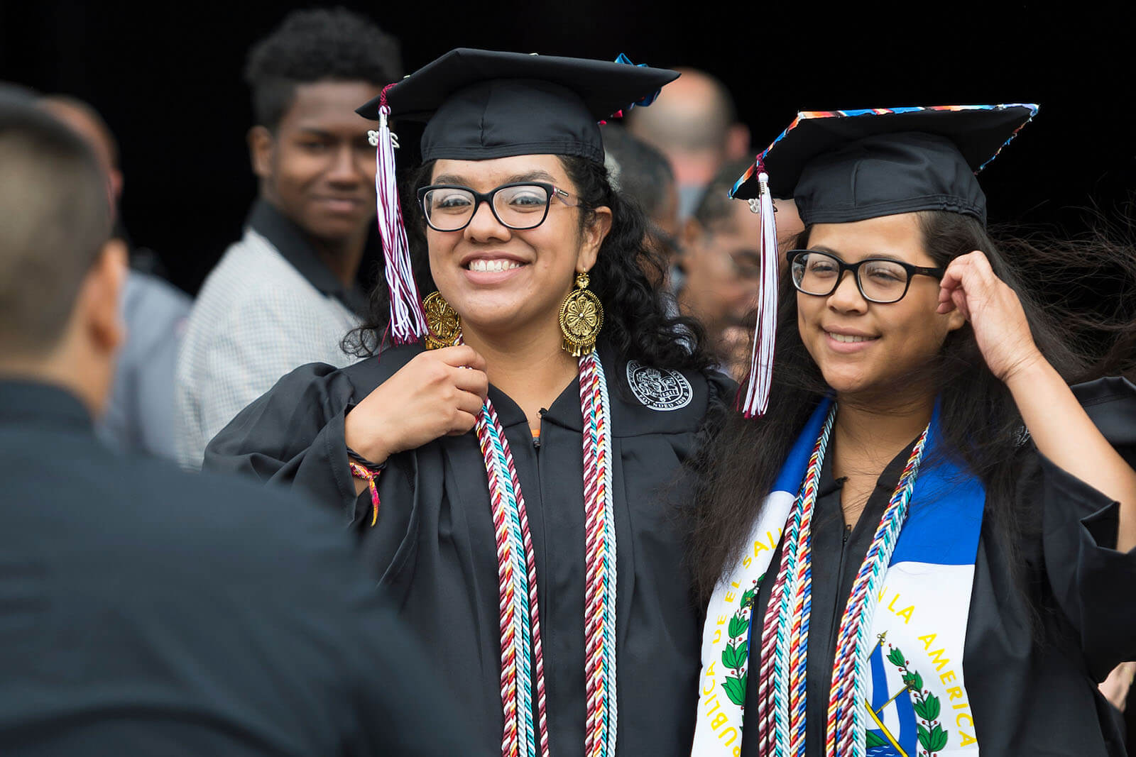 Student in cap and gown wreathed in flowers, beaming