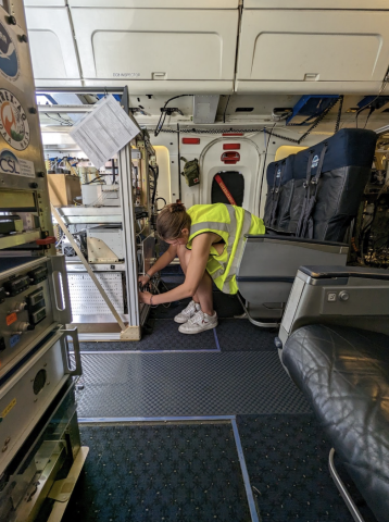 Photo of student Ekaterina Balsan '24 working on the plane while wearing a yellow, high visibility vest.