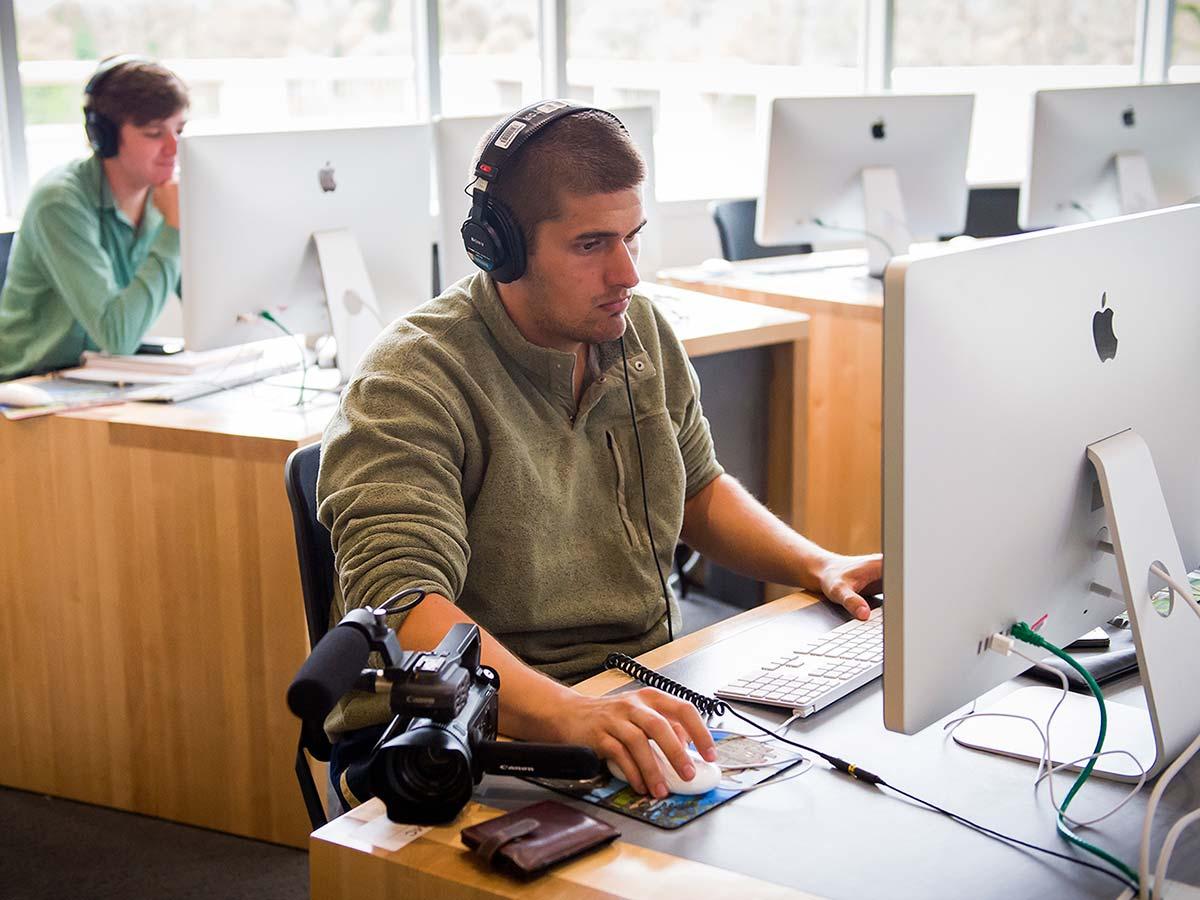 A student in headphones works with a computer and a camera in the Digital Learning and Media Center