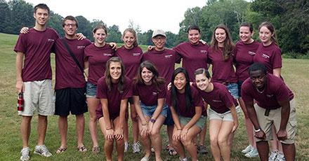 Two rows of students smile at camera and wear burgundy shirts.
