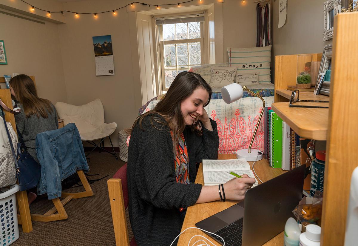 A student reads from a book at the desk in her room.