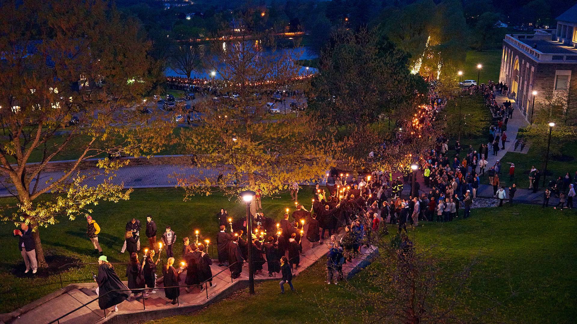 Students holding torches walk at night through campus