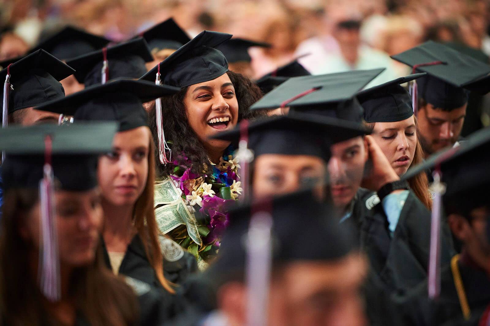 Student in cap and gown laughs during speaker’s remarks