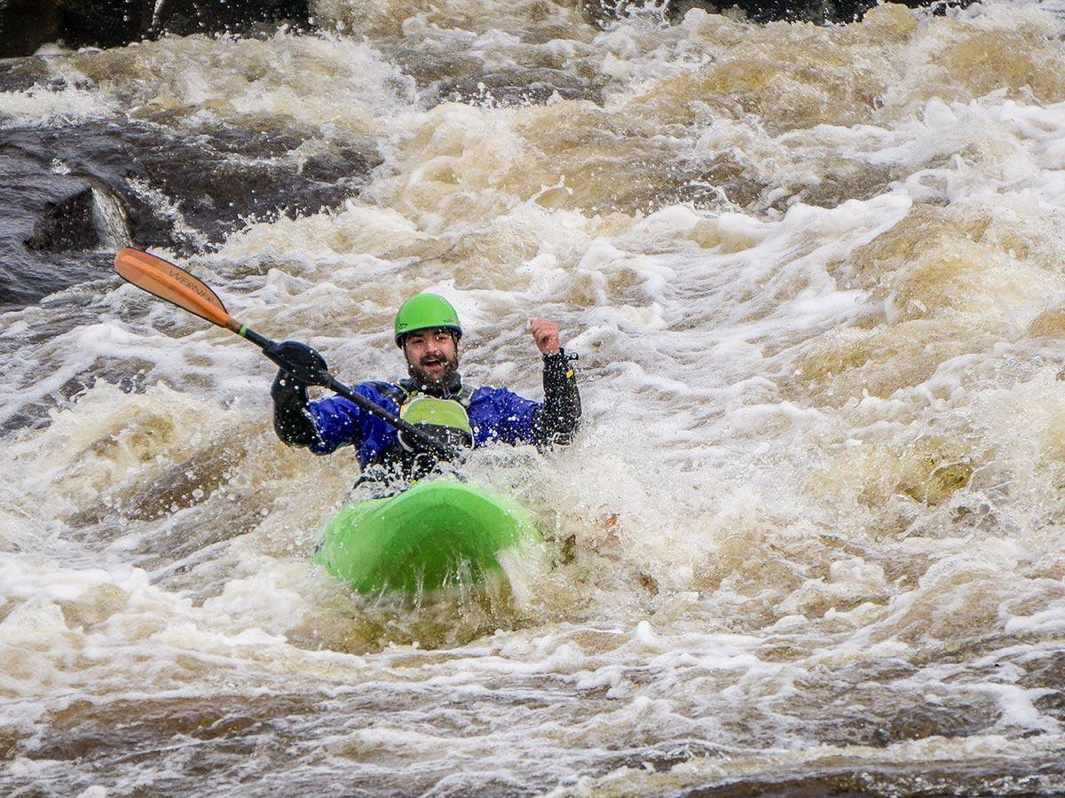 A student celebrates in his kayak after clearing a mid-stream rapid