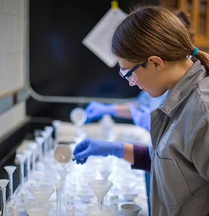 A student in protective gear, including goggles and gloves, in the laboratory
