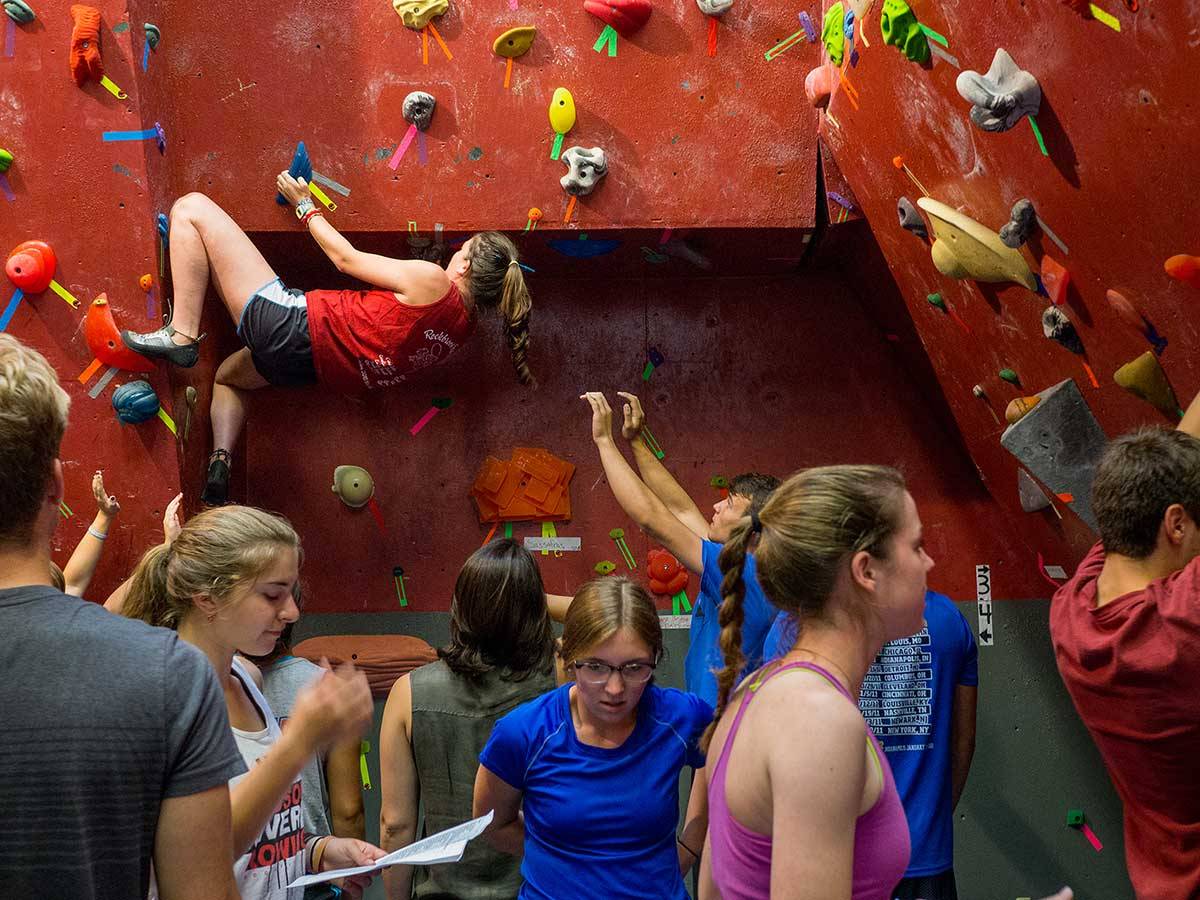 A female climbs in the background as students in the foreground prepare