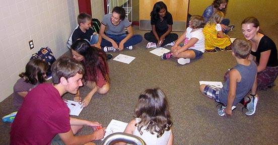 Colgate students speak with elementary students while sitting on the floor at Hamilton Central School