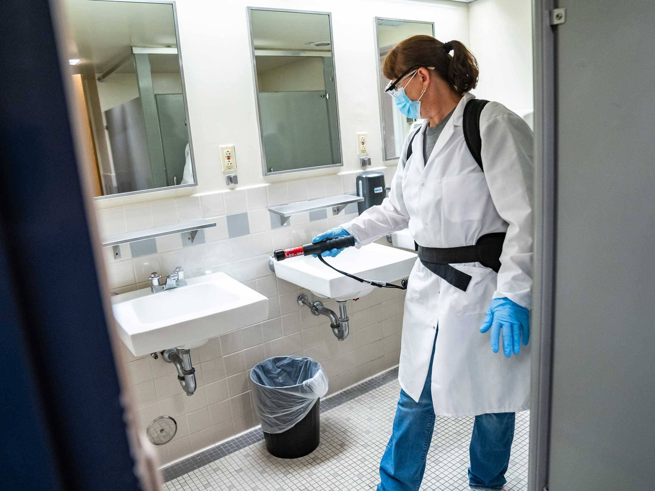 Staff member uses misting machine to clean bathroom surfaces