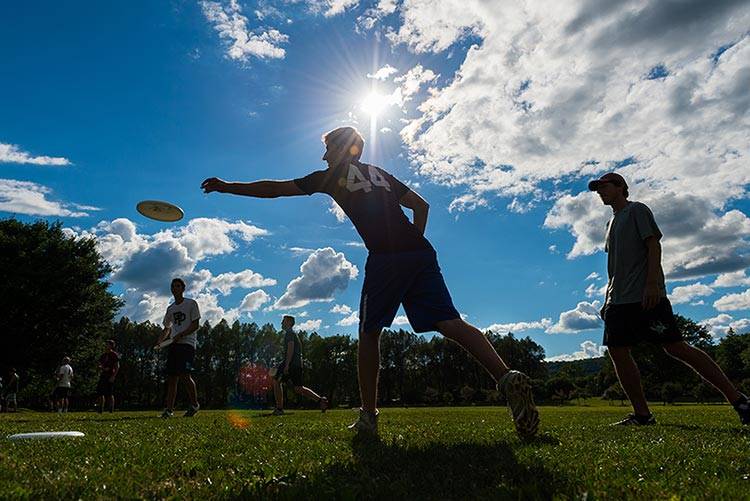 A student silhouetted in sunshine tosses a frisbee