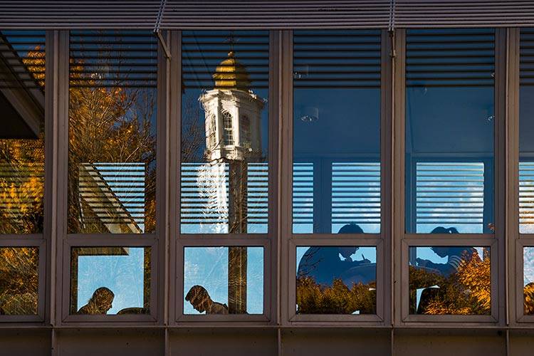 Colgate Memorial Chapel reflected off the windows of Persson Hall bridge as students work at tables inside