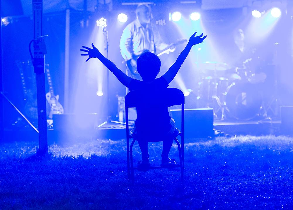 A child sits in a chair with arms raised at a concert during Reunion 2018