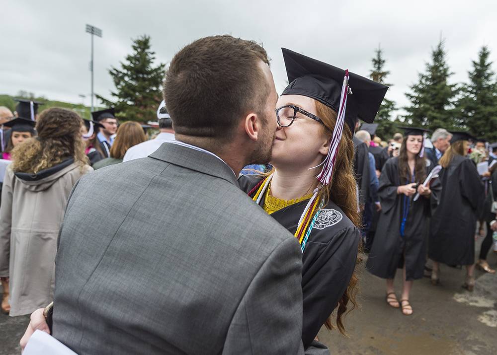 A couple, including a Colgate grad in cap and gown, kiss at Commencement