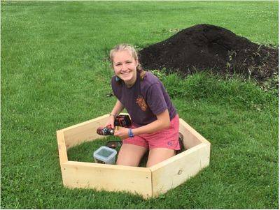 Grace is sitting around a wooden structure for her pollinator project