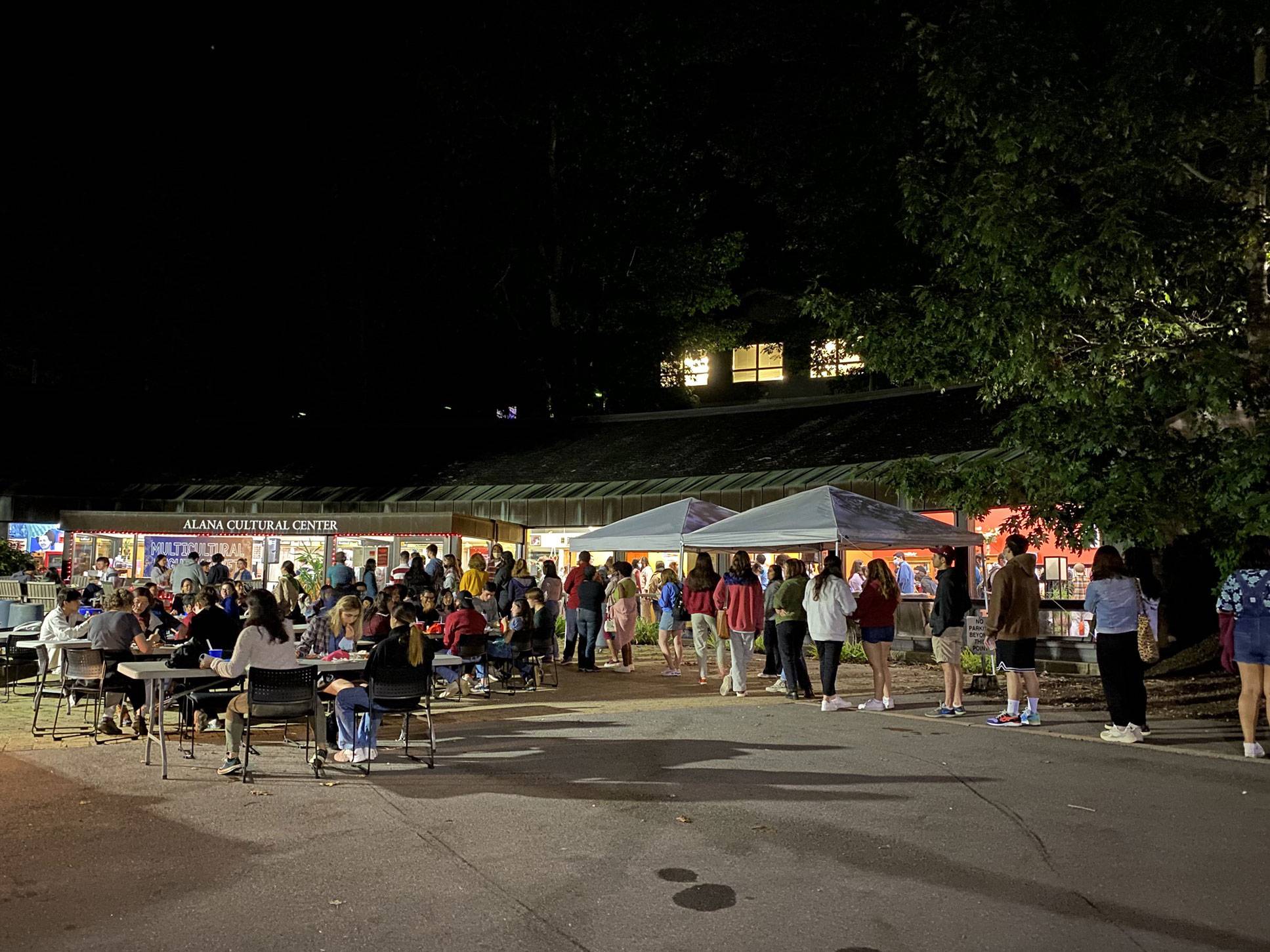 Students seated at tables and standing in line outside the ALANA Cultural Center at night time