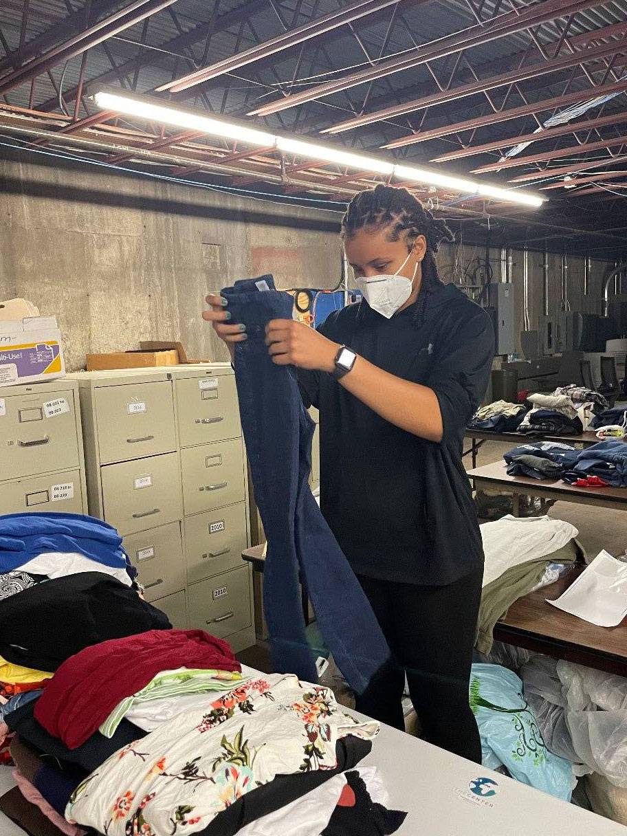 Tiasia McMillan folds a pair of jeans in the clothing storage room of the Center