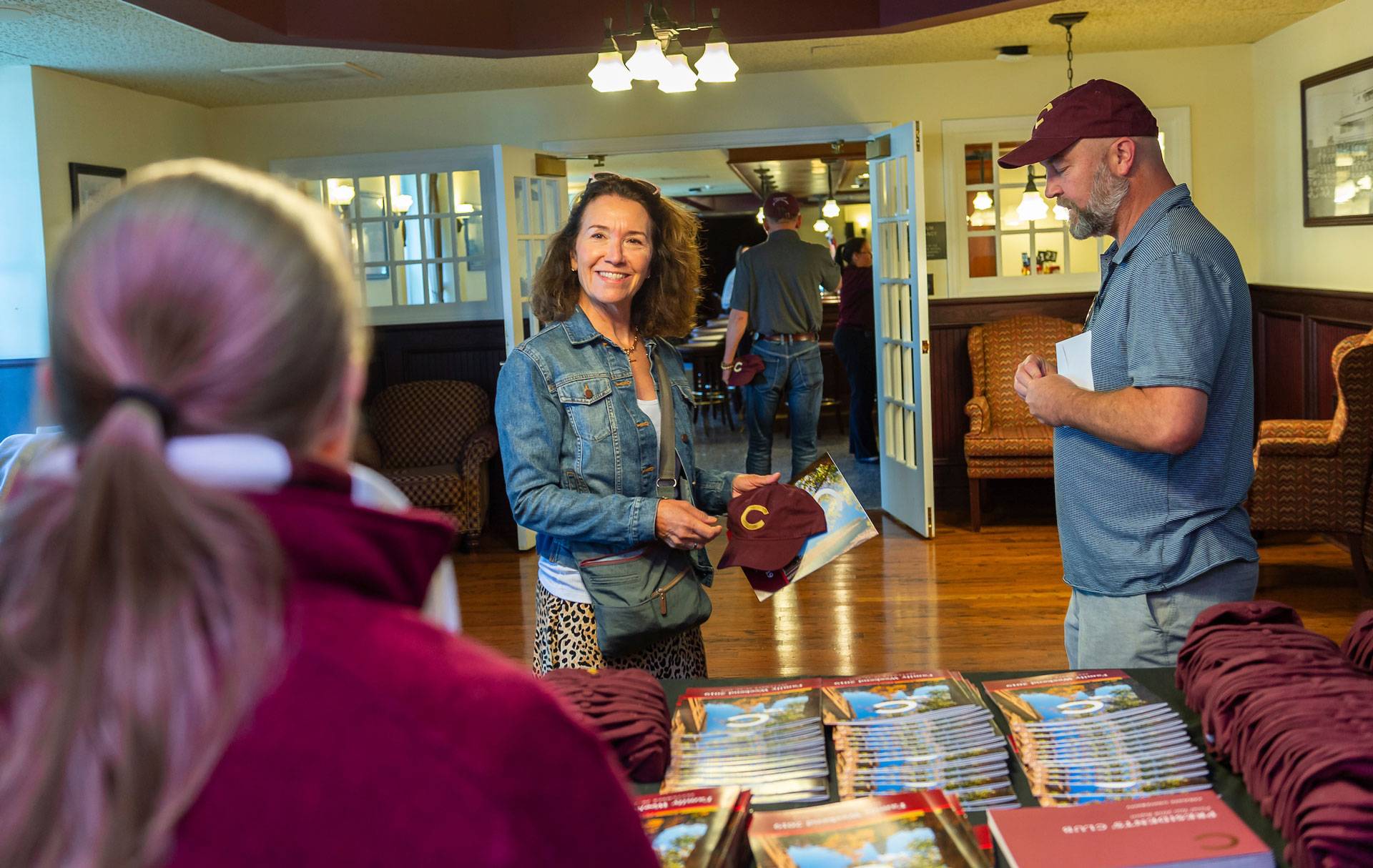 A mom in a jean jacket and dad in a Colgate baseball hat ick up a schedule at the welcome center table