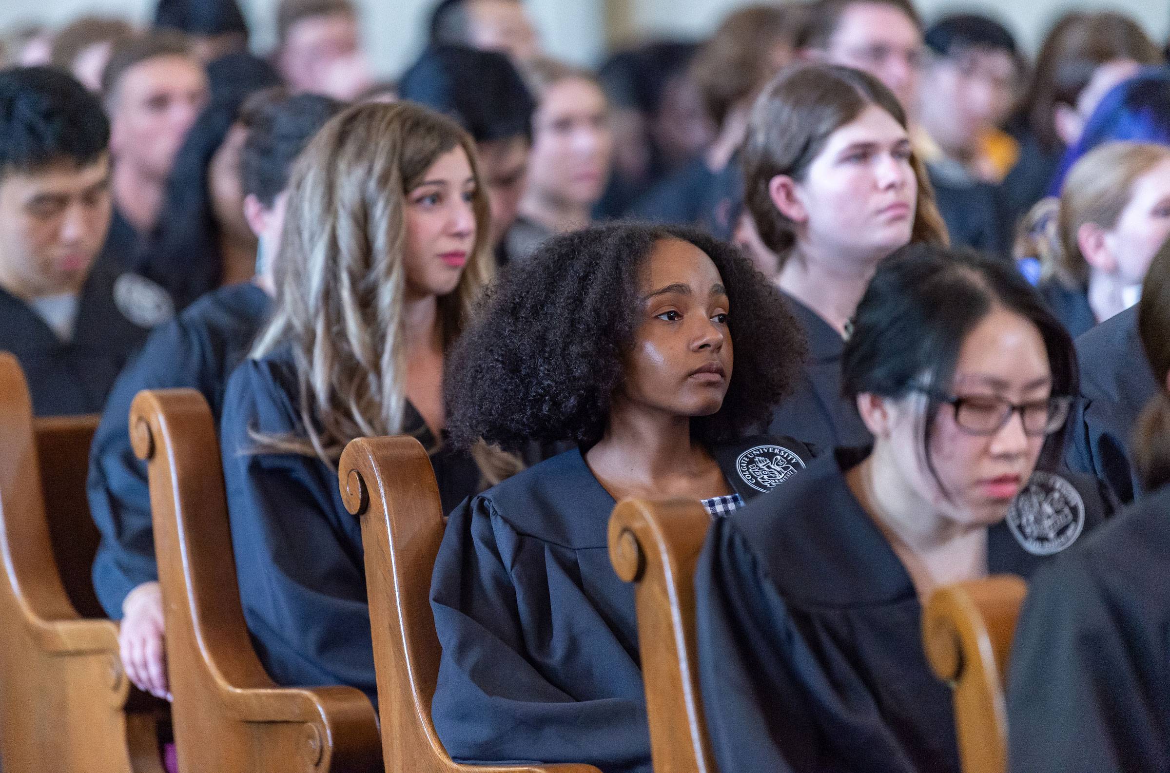 Students in commencement robes sitting in chapel pews watching the Baccalaureate Servcie