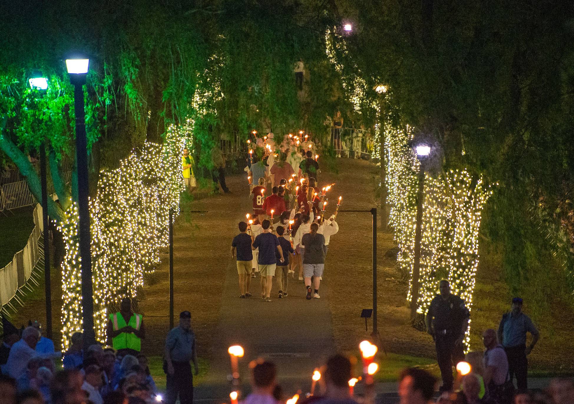 Graduates carrying torches proceed down the Willow Path, whose trees are strung with lights