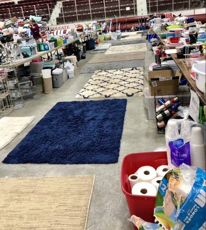 Photo showing rows of donated items, including rugs, lamps, cleaning supplies, and other household goods.