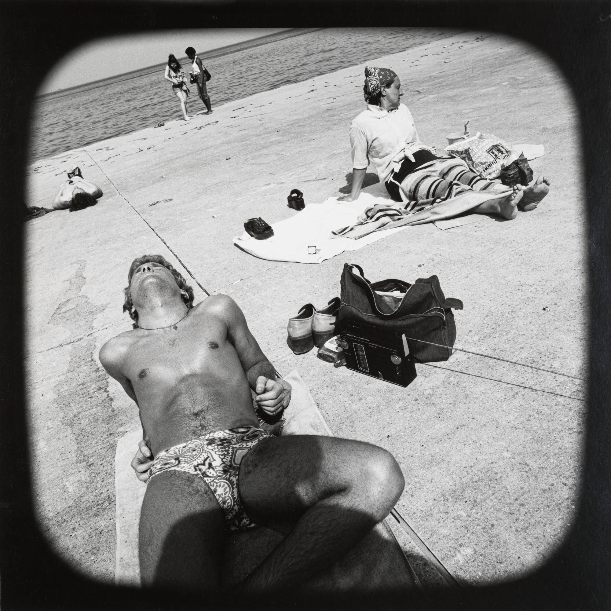 Scene at the beach focused on man on towel leaning back and looking up at the sun