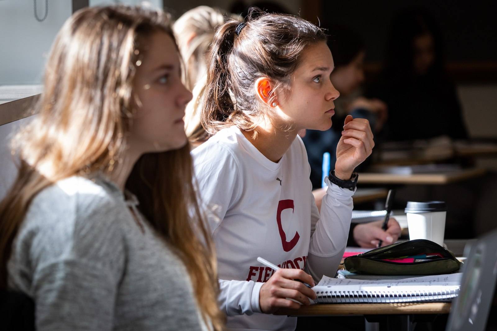 Two students listen to class lecture and take notes