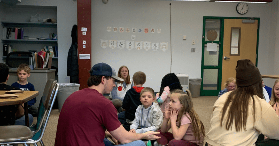 Colgate students sit and talk with small groups of elementary school students in a classroom