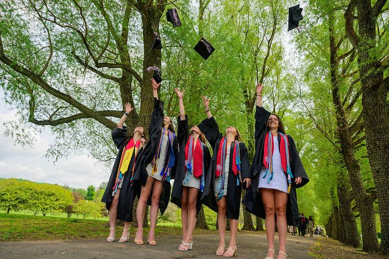 A group of graduates toss their caps into the air as they stand on Willow Path