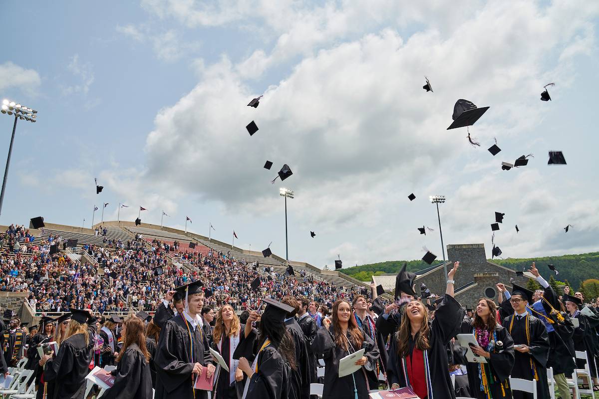 After commencement, some graduates smile and throw their caps into the air as others prepare to exit the football stadium.