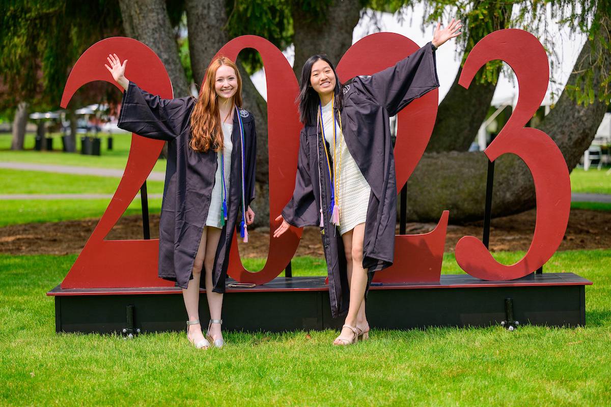Two Colgate graduates stand in front of a large red 2023 sign.
