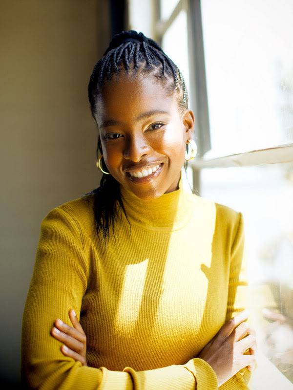 Portrait of Amanda Gorman standing with arms crossed near a window