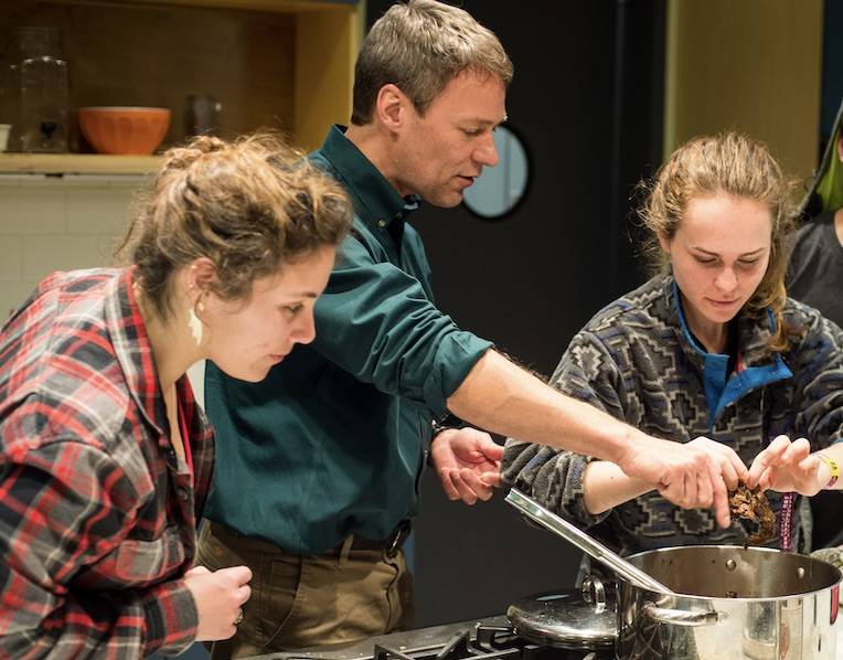 Professor Ian Helfant putting ingredients into a pot as students look on.