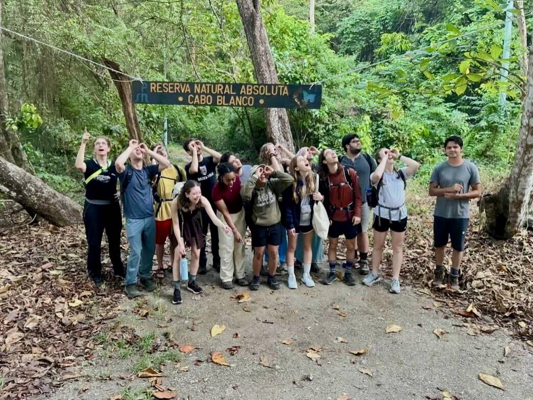 A group of students posing with binoculars on the forest floor.
