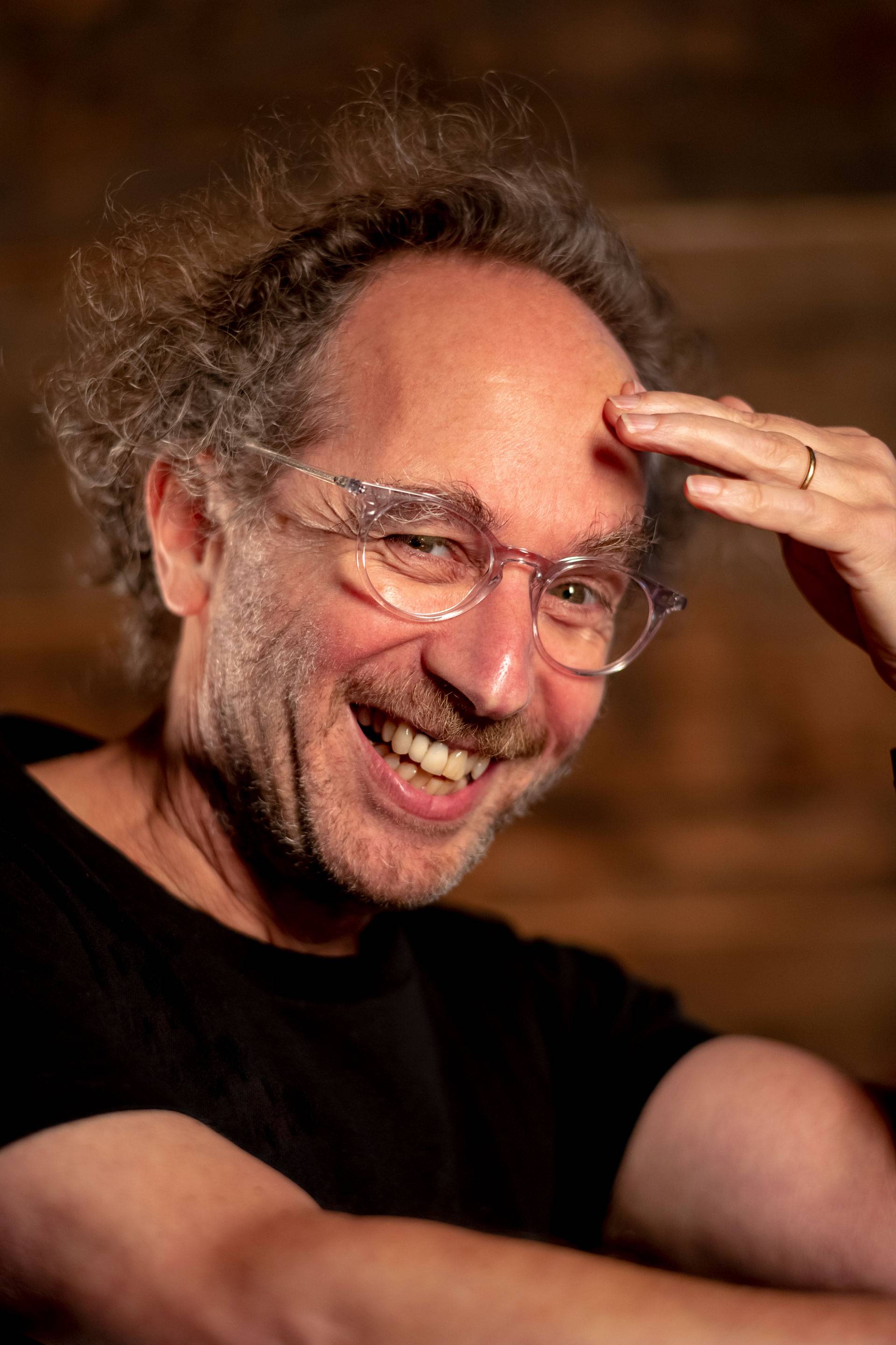 Portrait of Tod Machover. He is smiling from the side, wearing a black t-shirt and has one hand to his forehead