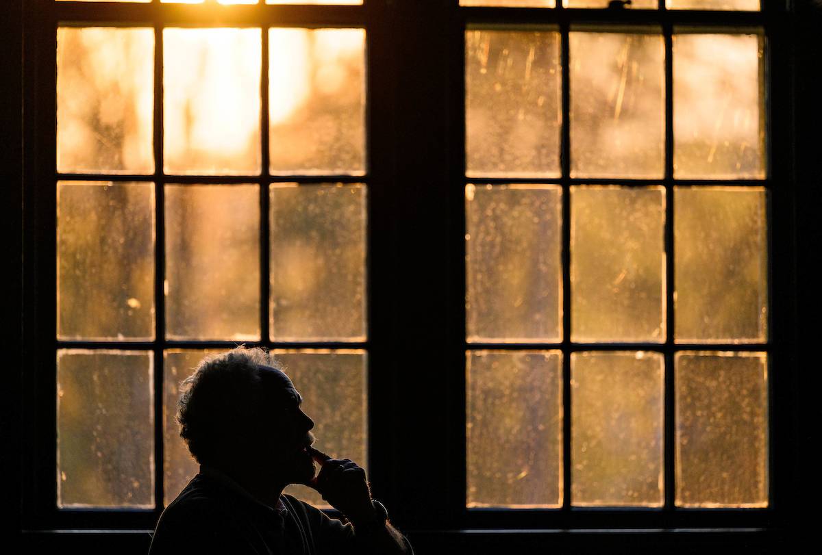 A man sits besides a backlit window at sunset