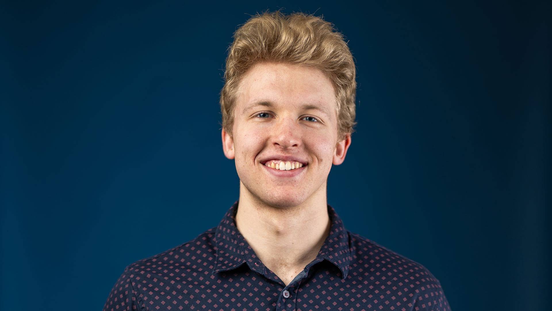 Corrigan Peters standing in front of a blue background.