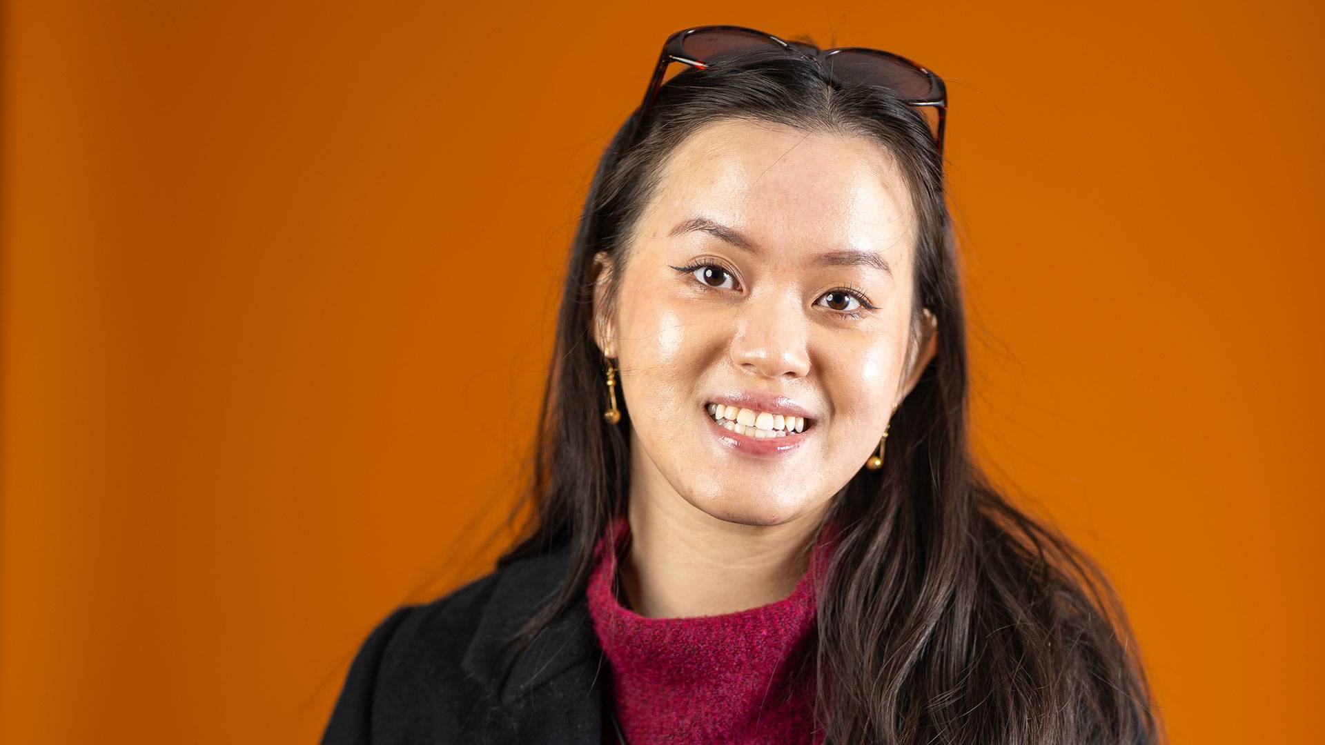 Linh standing in front of an orange background.
