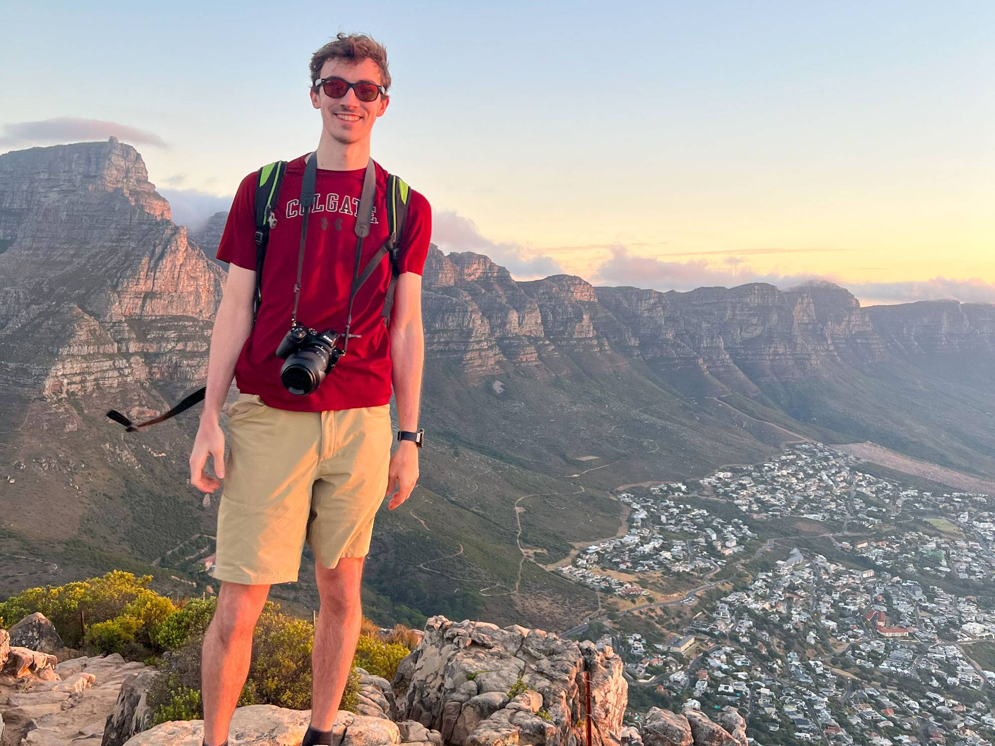 Gio Cavalli ’24 stands on cliff with mountains behind and city below