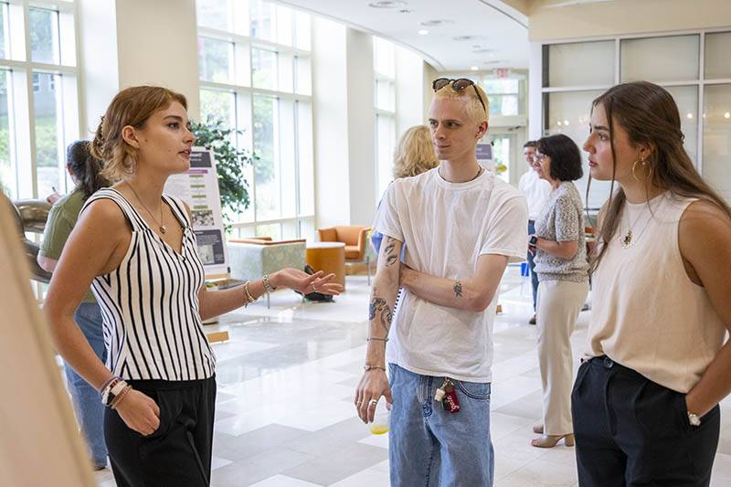 A student presents their research poster to two attendees