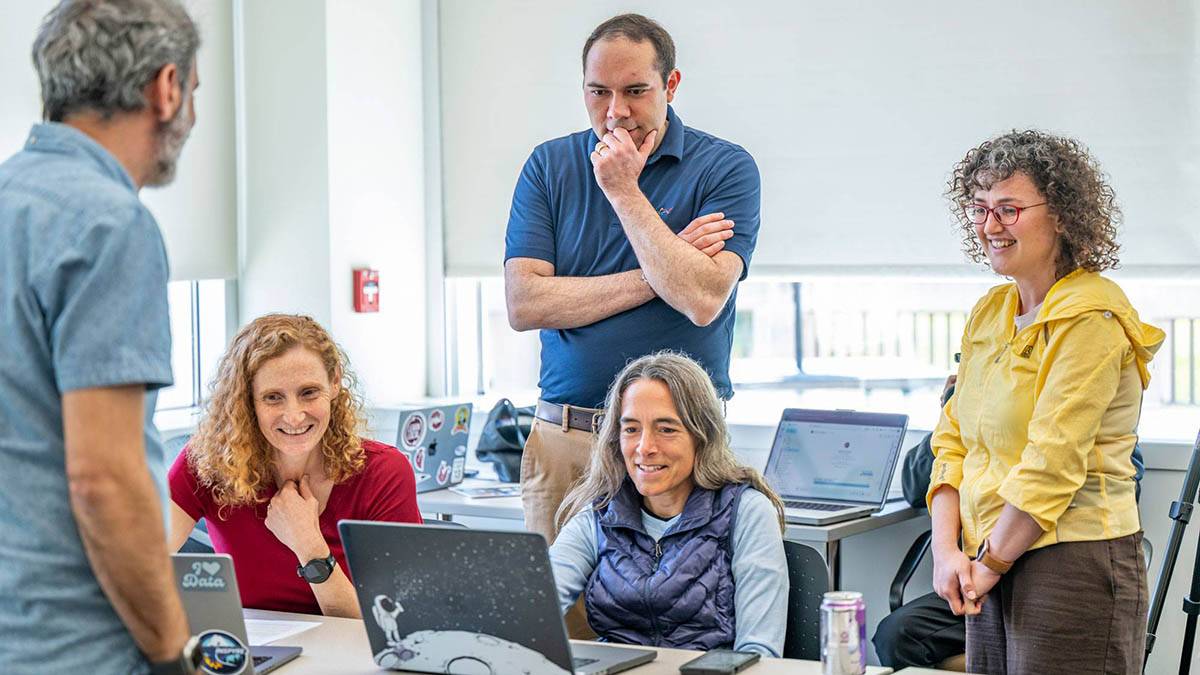 A group of professors converse around a laptop