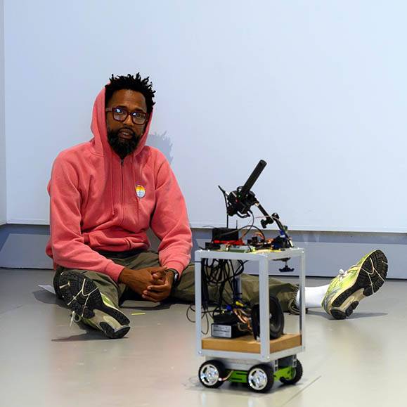 An actor sits on the floor near a robot