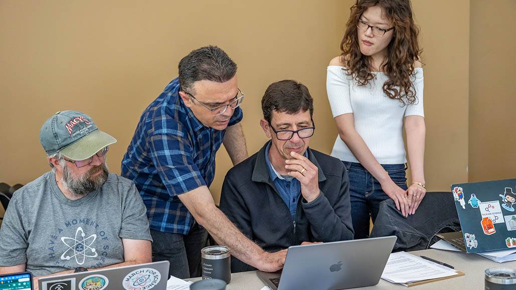 A group of professors look at another's laptop