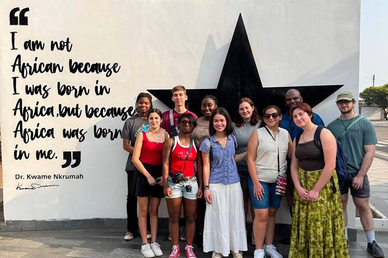 11 students pose for a photo in front of a mural wall