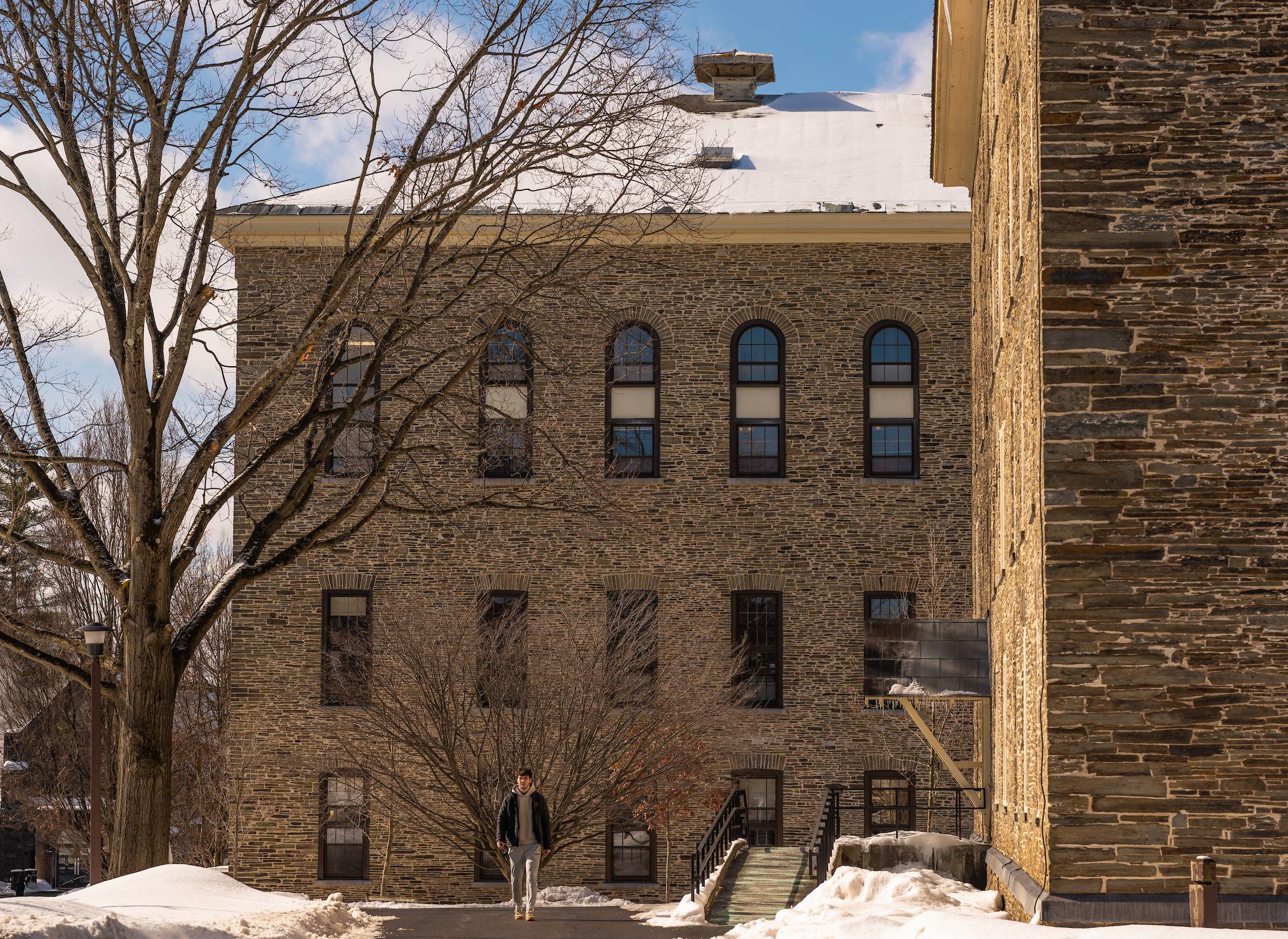 On a sunny morning with snow on the ground, a student walks on a path on the Academic Quad with an accessibility ramp to their left.